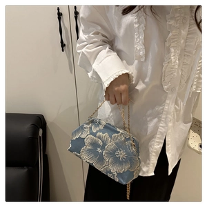 Detail of light blue shell bag with white flower embroidery and gold chain strap