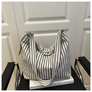 Detail of blue and white striped canvas tote bag with wide shoulder strap on decorative book