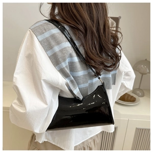 Rear view of model wearing a glossy black faux leather underarm bag in a warm room