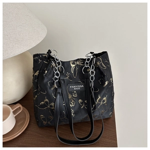 Détail d'un sac cabas en tissu noir avec broderies papillons dorées et chaîne