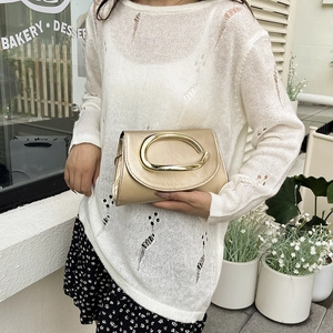 Sac bandoulière tendance champagne doré avec fermoir en C présenté dans un décor de café