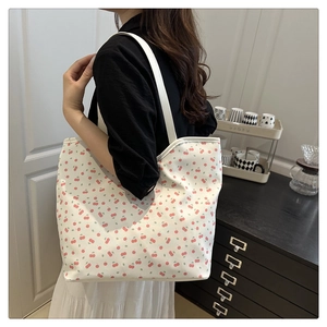 Close-up of a large white canvas tote bag with pink cherry prints on a model's shoulder