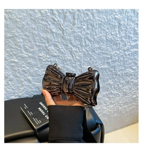 Detail of a black butterfly-shaped clutch bag in glossy patent finish with gold chain