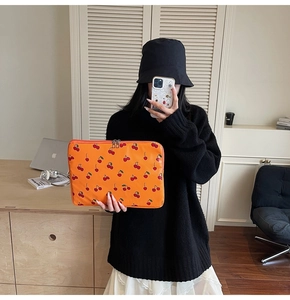 Detailed close-up of orange laptop sleeve with red cherry pattern and metal zipper closure