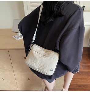 Detailed view of cream nylon crossbody bag with pleated texture and silver flower charm