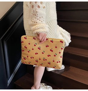 Detail of laptop sleeve with cherry print patterns and zipper closure in model's hand