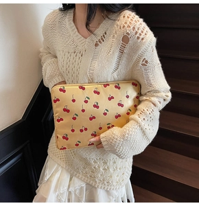 Detail of satin yellow clutch bag with cherry pattern and golden zipper closure