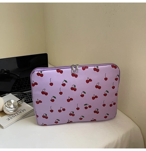 Close-up of lilac laptop sleeve with cherry print and dual metal zippers on a desk