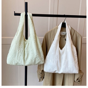 Détail de la broderie florale sur des sacs cabas en coton vert doux et blanc