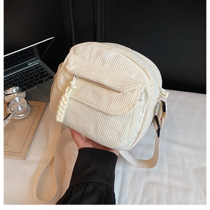 Detail of white corduroy crossbody bag featuring a textured flap pocket and woven zipper pull