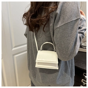 White mini crossbody bag with a rectangular flap and long adjustable strap on a person