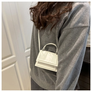 Detail of a white mini PU leather trapezoid handbag worn by a model with thin shoulder strap