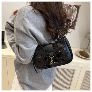 Detail of black sequined shoulder bag featuring leather strap and golden metallic clasp