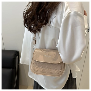 Détail d'un sac selle beige avec surpiqûres en losanges et lettrage sur le rabat