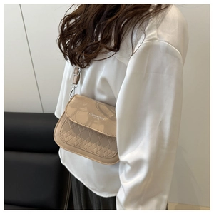 Détail du sac bandoulière beige avec texture matelassée et lettrage contemporain