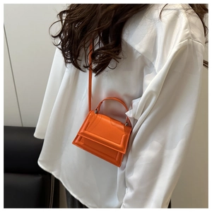 Detail of an orange leather mini square bag with top handle and crossbody strap