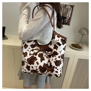 Detail showing cow print pattern and brown bow decoration on a large shoulder tote bag