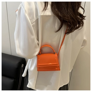 Rear view of model wearing an orange mini PU leather crossbody bag with a magnetic flap