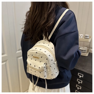 Close-up of a mini cream-white quilted backpack with black print and metal Fashion logo