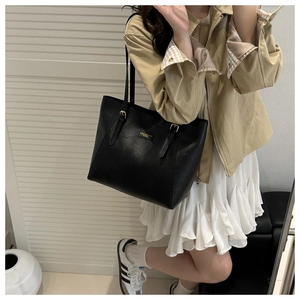 Détail d'un grand sac cabas noir en similicuir avec boucles dorées et logo sur le devant
