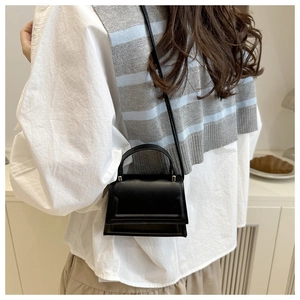 Close-up of a black minimalist mini bag worn over a white shirt and grey knit vest