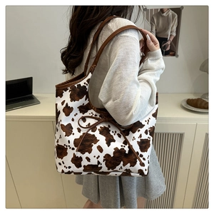 Detail of a large cow print tote bag with brown faux leather straps and bow accent