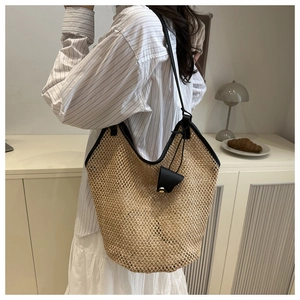 Close-up of woven straw tote bag with black leather trim and triangle pendant detail
