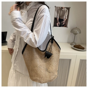 Detail of handwoven straw tote bag with black leather straps and hanging charm