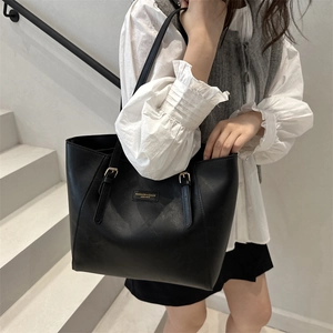 Grand sac cabas en cuir noir avec logo doré porté par un mannequin dans un décor