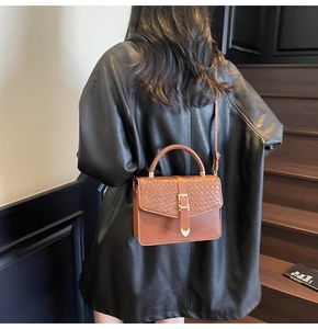 Détail d'un sac à main marron en cuir tressé avec boucle cœur dorée porté sur un manteau