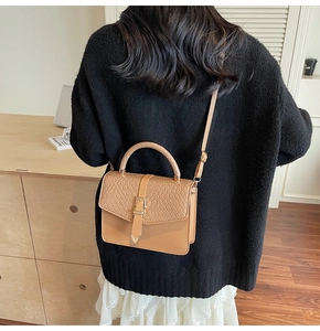 Détail du rabat tissé et de la boucle dorée sur un sac bandoulière porté par un mannequin