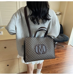 Detail of a large brown monogram tote bag with embossed M logo and long shoulder strap