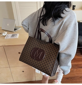Brown tote bag with vintage M-pattern print and long shoulder strap in daily usage