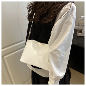 Detail of white glossy shoulder bag featuring a gold metal plaque and sleek trapezoid design