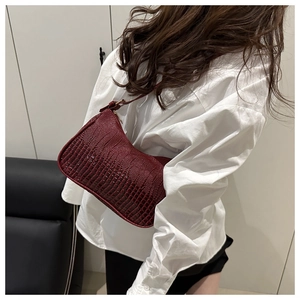 Detail shot of a burgundy faux leather underarm bag with a vintage crocodile texture