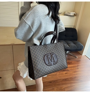 Brown tote bag with letter print pattern and embossed logo shown in a lifestyle setting