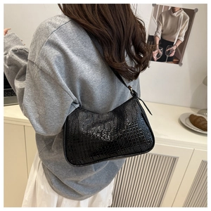 Close-up of black crocodile pattern shoulder bag on model in a minimalist setting