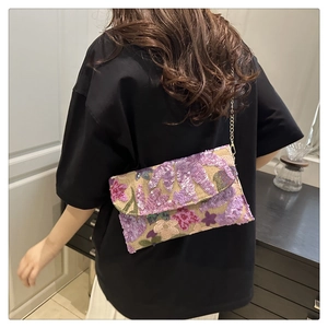 Detailed macro view of sequin floral embroidery on women's envelope straw woven handbag