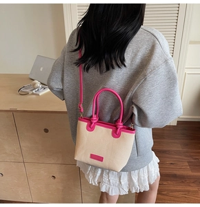 Detail of pink leather handles and straw woven texture on a versatile crossbody bucket bag