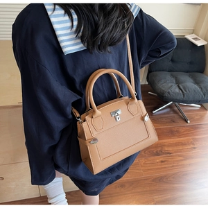 Close-up of brown pebbled leather handbag with silver lock being held in a home setting