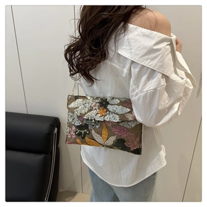 Close-up of bohemian envelope bag with floral sequin embroidery and gold chain strap