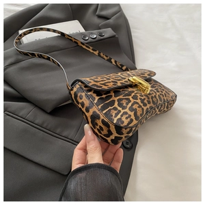 Detail of leopard print baguette bag with golden metal twist lock on a grey suit