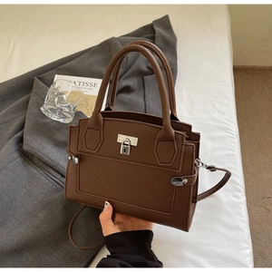 Detail of dark brown lychee grain leather handbag with silver twist lock on soft bedding