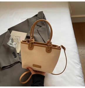Detail of beige straw woven tote bag featuring brown leather handles and brand label tag