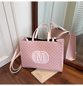 Close-up of pink tote bag with M-letter prints, metal logo, and long shoulder strap