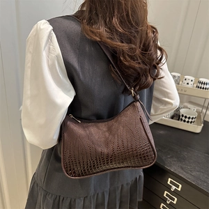 Brown crocodile embossed shoulder bag worn by model in a minimalist interior setting