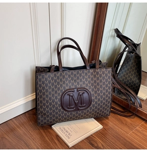 Detail of vintage tote bag with M-pattern print and large 3D embossed logo accent