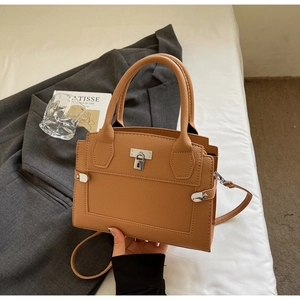 Close-up of camel brown textured leather handbag with silver padlock and metal hardware