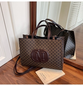 Detailed close-up of dark brown tote bag with M-monogram pattern and circular leather logo