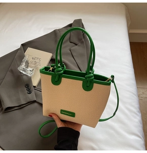 Detail of woven tote bag with green leather trim and handle on a neutral background